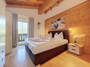 A bedroom with a wooden ceiling, a bed with white bedding, a nightstand with a lamp, and a view through a glass door. - Kitzsteinhorn am See by Interhome (Zell am See)