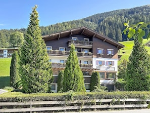 A multi-story hotel with balconies, surrounded by greenery and a mountainous backdrop. - Kitzsteinhorn am See by Interhome (Zell am See)