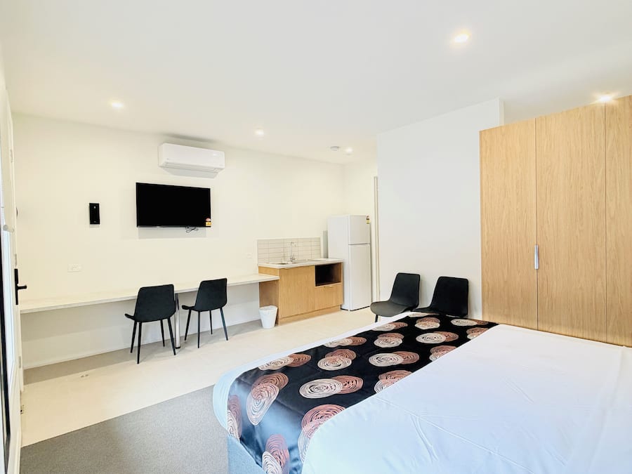 Ein modernes Hotelzimmer mit einem großen Bett, einem Schreibtisch mit Stühlen, einem Fernseher und einem Kleiderschrank.