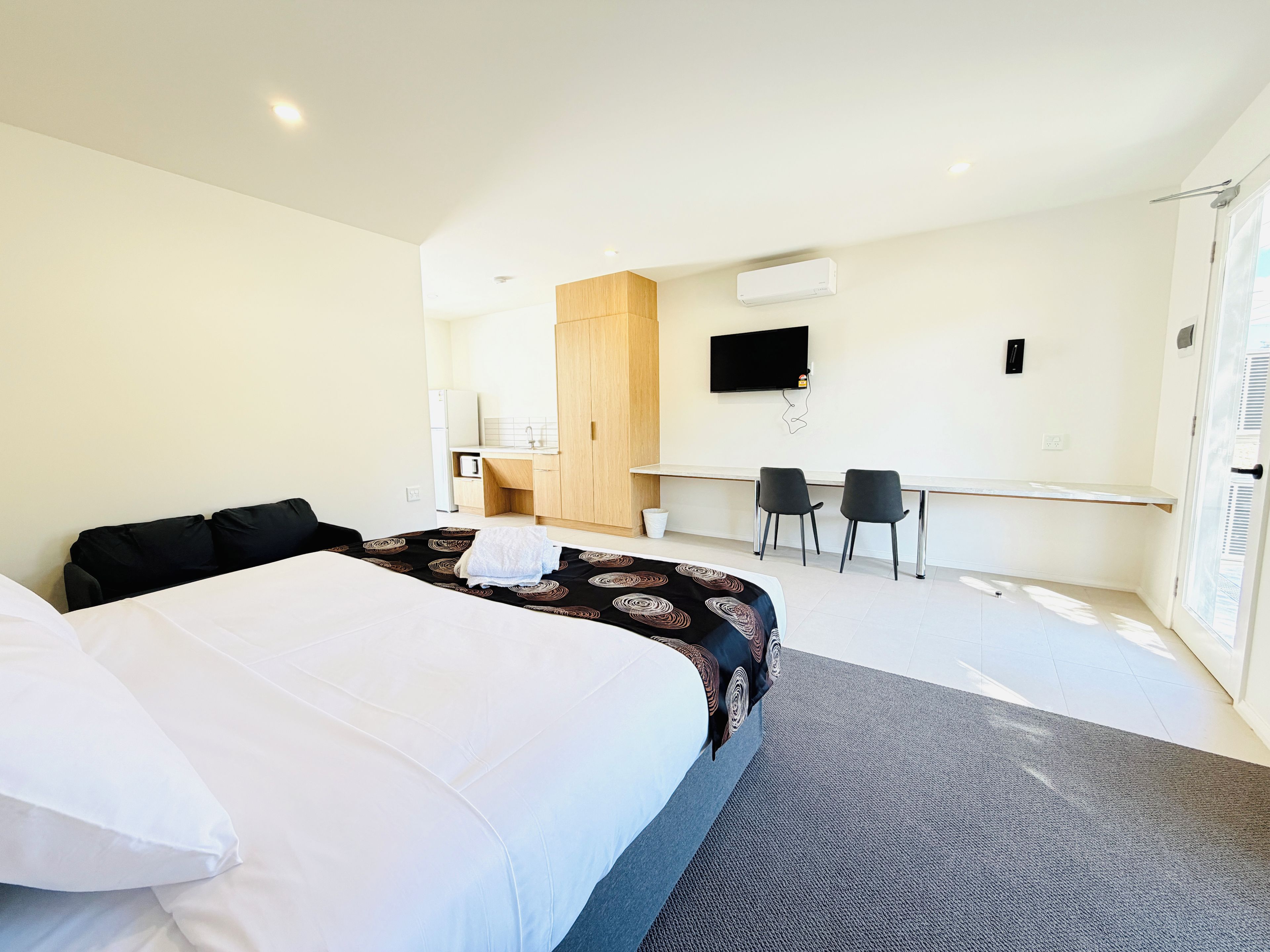Una habitación de hotel con cama, escritorio, dos sillas, televisión y armario.