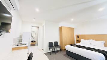 Una habitación de hotel con cama, escritorio, silla, espejo y armario.