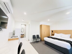 A hotel room with a bed, a desk with a chair, a mirror, and a wardrobe.
