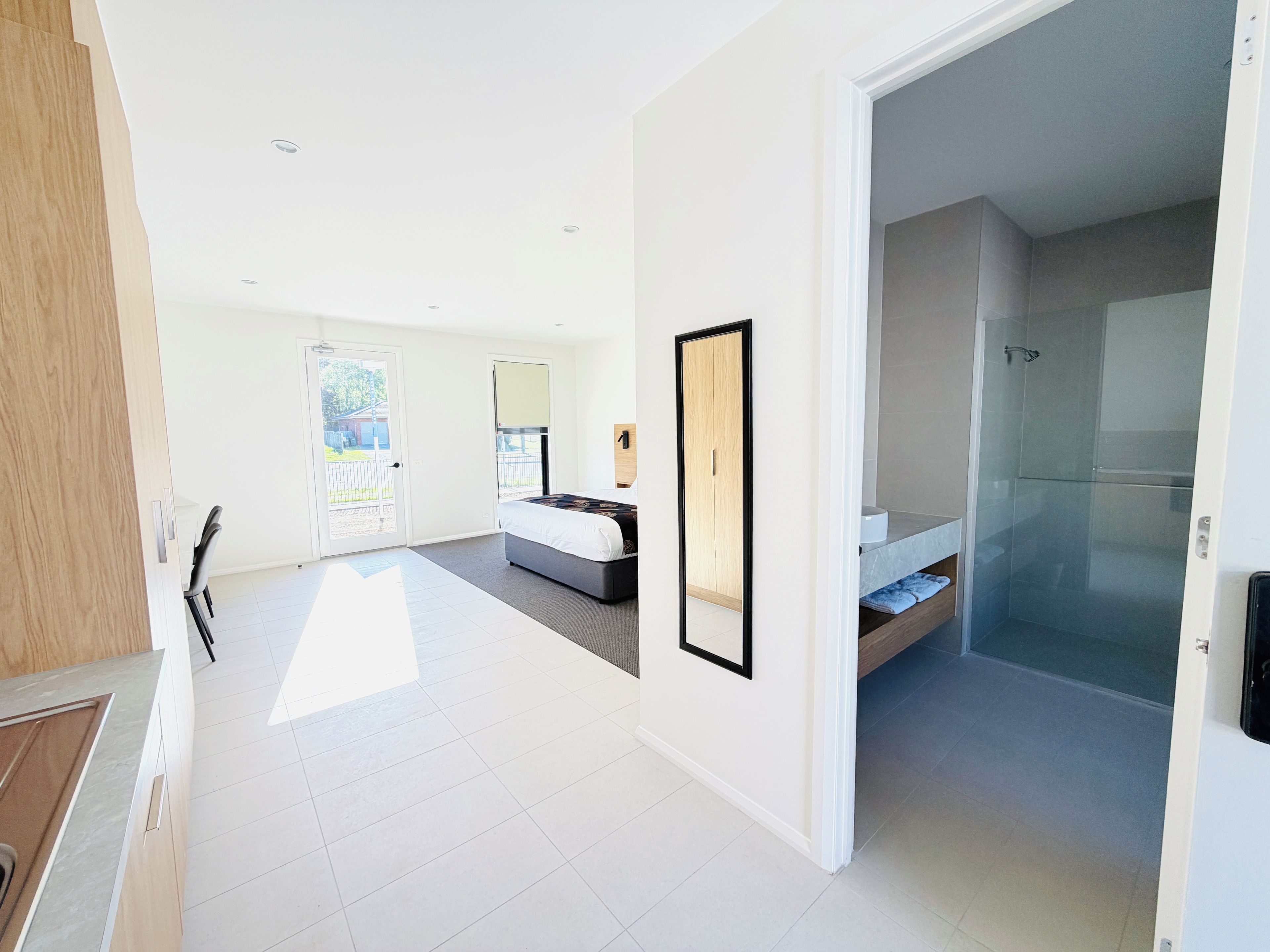 A modern hotel room with a large bed, a bathroom with a glass shower, and a view of the outdoors.
