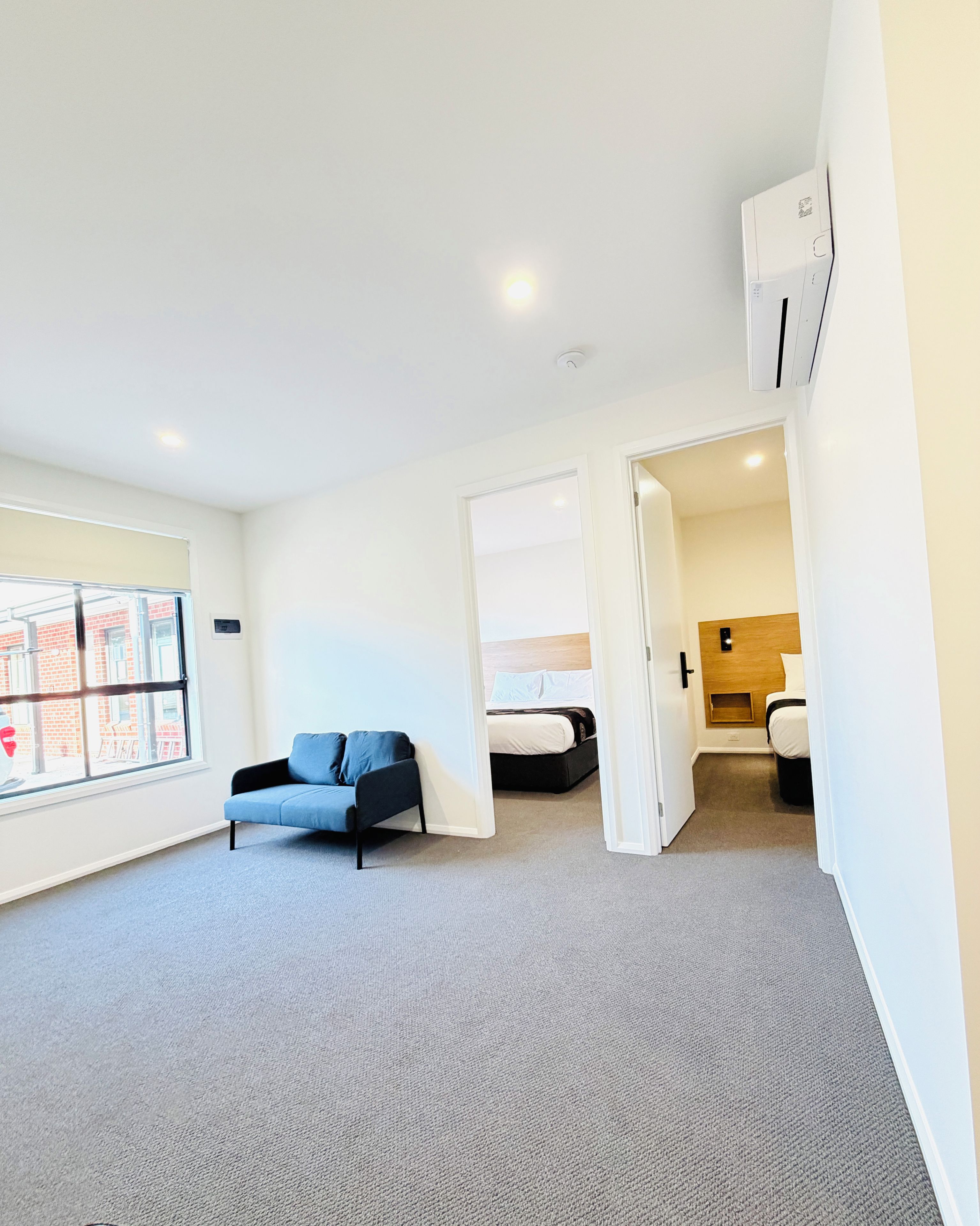 Habitación de hotel moderna con sofá, cama y baño a la vista a través de una puerta abierta.