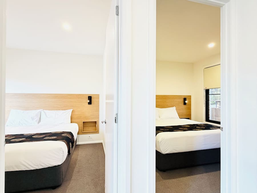 A hotel room with two beds, a wooden headboard, a carpeted floor, and a window with a view.