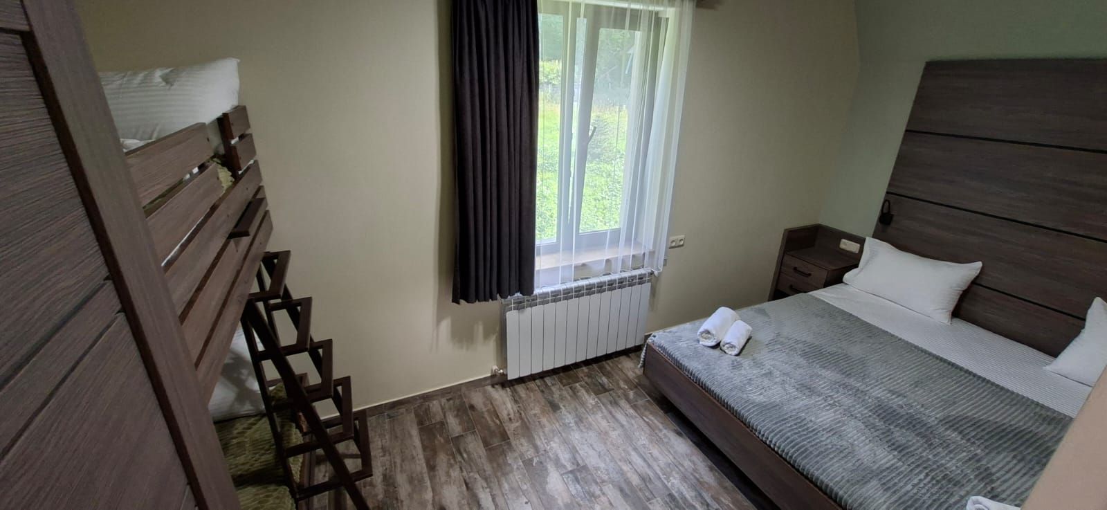 Una camera da letto con un letto, un comodino, una scala in legno, una finestra con tende e un termosifone.