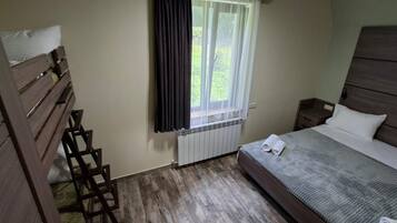 Una camera da letto con un letto, un comodino, una scala in legno, una finestra con tende e un termosifone.