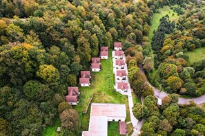 An aerial view of a residential area with multiple houses, a central road, and surrounding greenery.