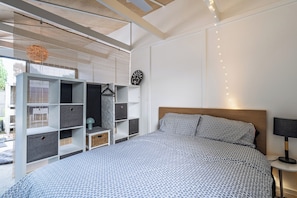 A modern bedroom with a large bed, built-in shelving, a hanging light fixture, and a wall clock. - Cottesloe Coastal Escape | Fire Pit & Games (Barwon Heads)