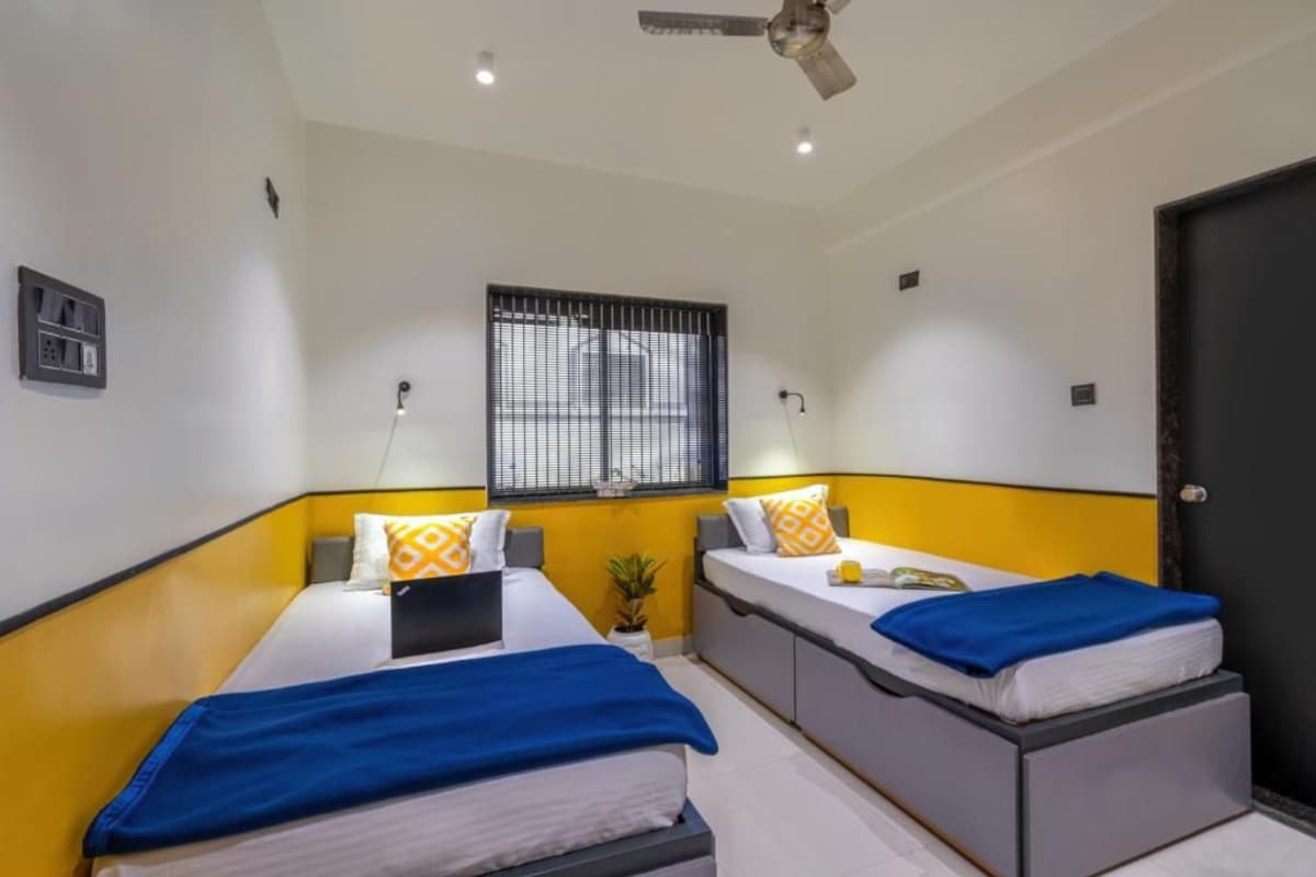 A hotel room with two beds, a ceiling fan, a window with blinds, and a door.