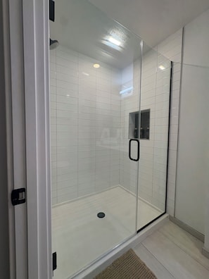 A glass-enclosed shower with white tiles and a visible drain.