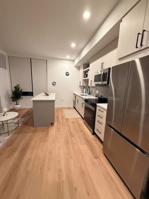 A modern kitchen with a central island, stainless steel appliances, and light wood flooring.