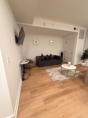 A living room with a sofa, a round coffee table, and a TV mounted on the wall.