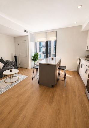 A modern kitchen with a central island, bar stools, and a view of the city through large windows.
