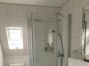 A modern bathroom with a glass shower enclosure, a toilet, and a vanity with a mirror. - Flurstrasse - OG Links (Wyk auf Foehr)