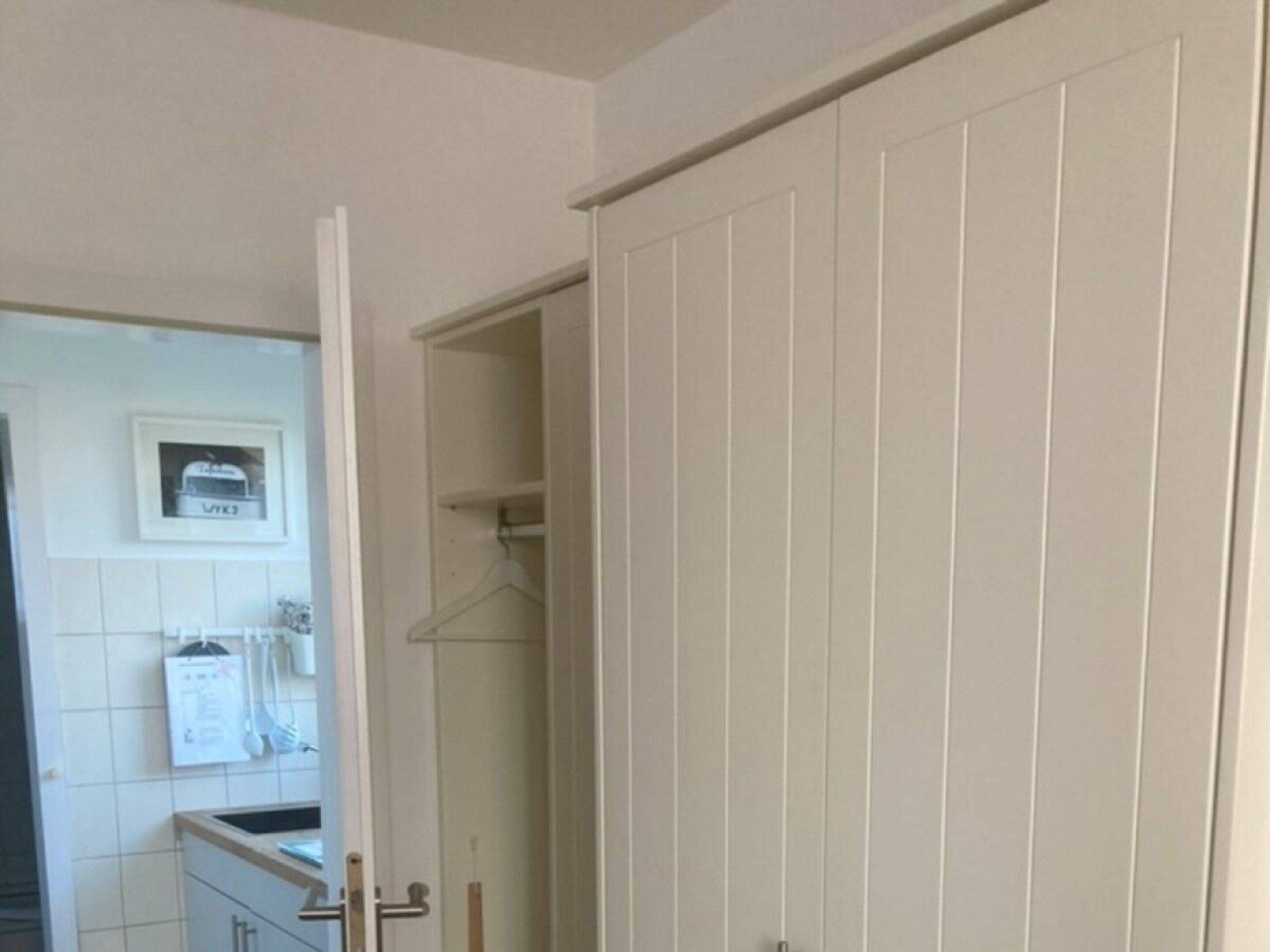 Een kamer met een kledingkast, een deur naar een andere kamer en een handdoekhouder aan de muur.