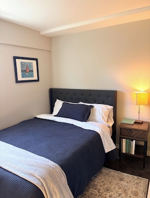 A neatly made bed with a dark headboard, a bedside lamp, and a framed picture on the wall.