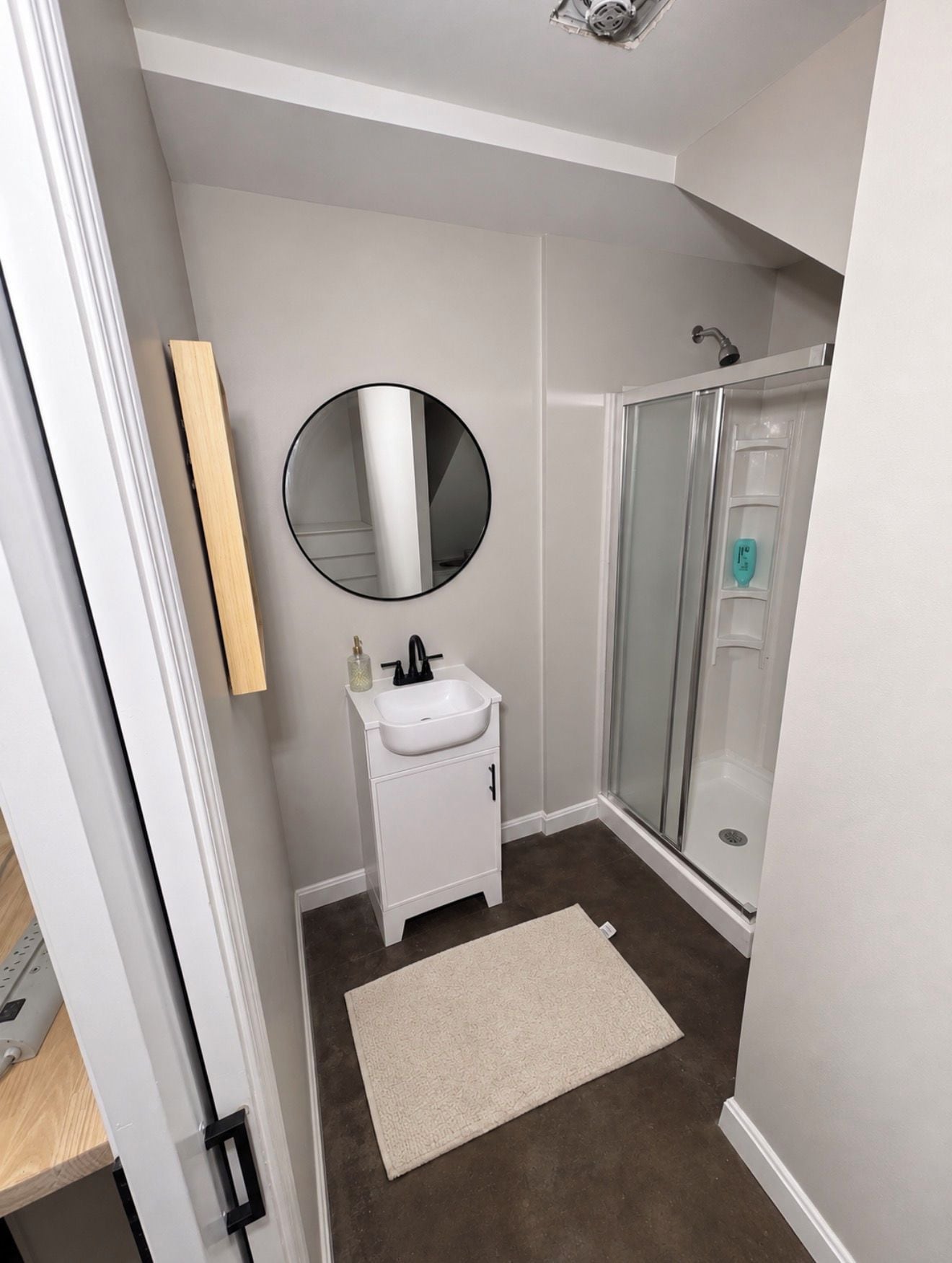 Un baño con un lavabo blanco, un espejo redondo, una cabina de ducha y una alfombra color beige.
