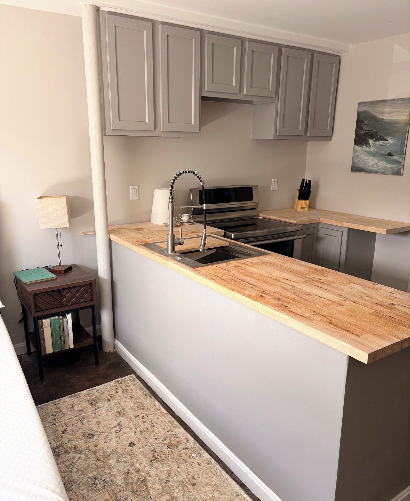 Una cocina moderna con armarios grises, encimera de madera, estufa integrada y un lavamanos.