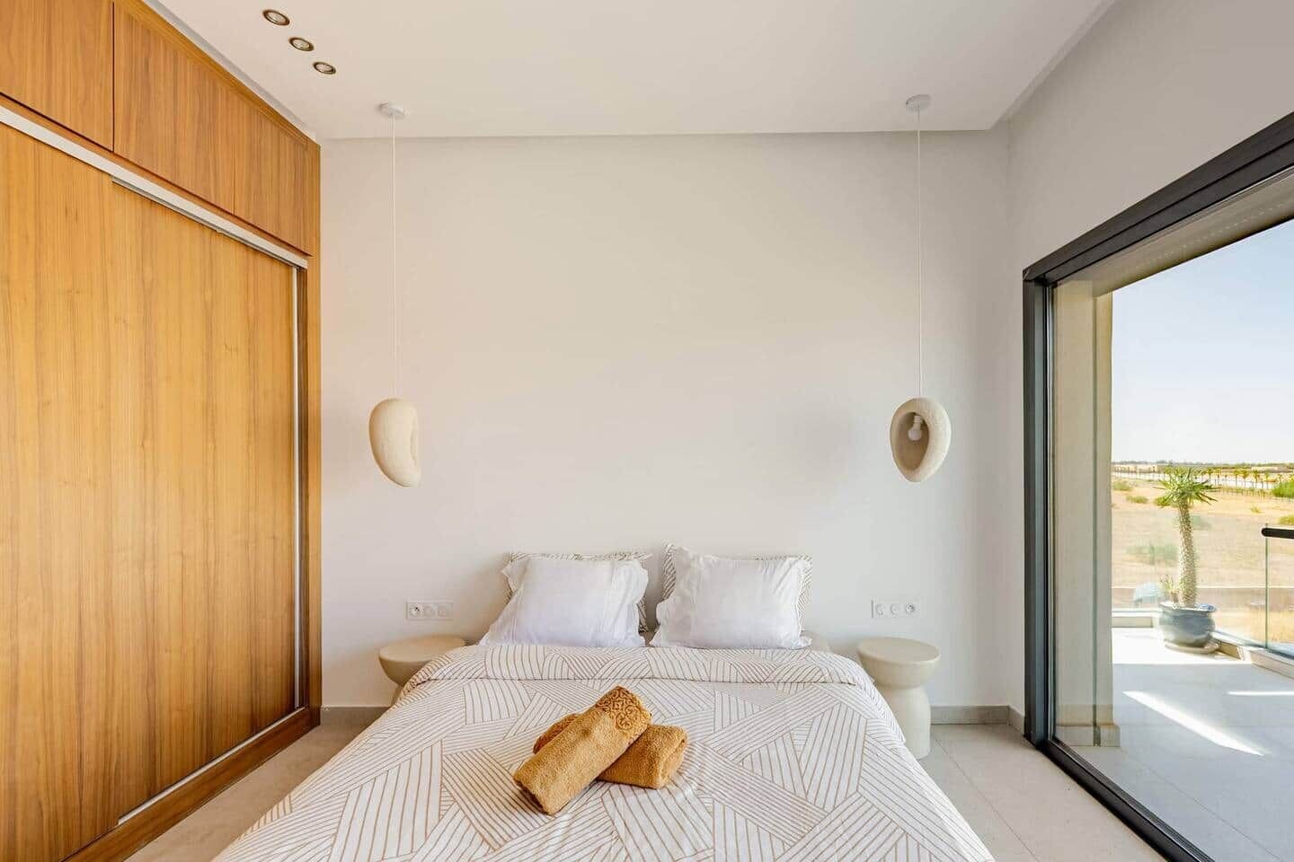 A modern bedroom with a large bed, a wooden wardrobe, and a view of the desert through a large window.
