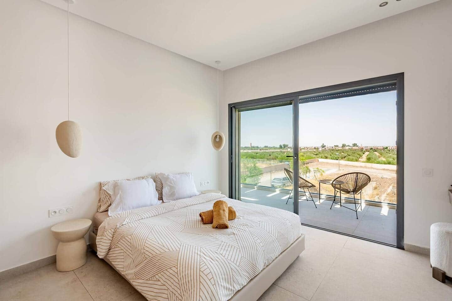 Une chambre moderne avec un grand lit, une vue sur l’extérieur et un balcon équipé de chaises.