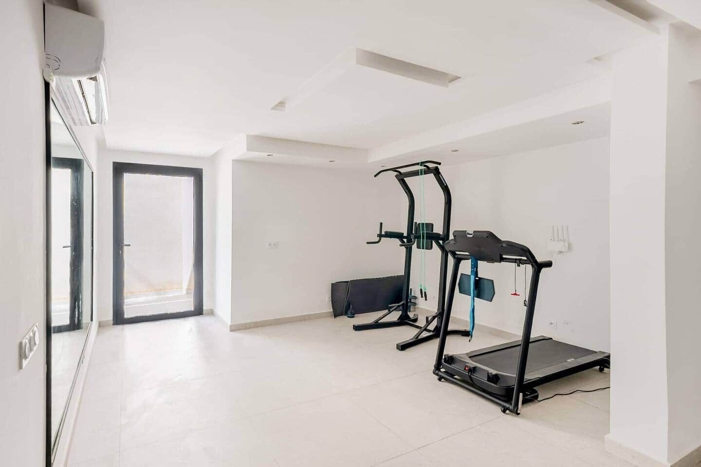 Une pièce spacieuse équipée d’un tapis de course, d’un vélo d’appartement et d’un banc.
