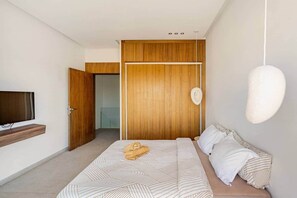 Una camera da letto moderna con un letto, una TV a parete e un'armadio in legno.