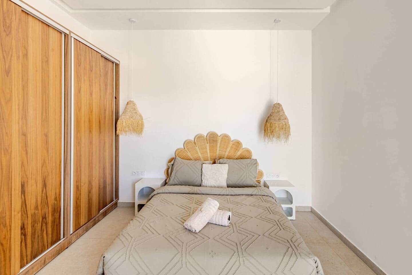 A bedroom with a bed, a wardrobe, and two wall-mounted lamps.