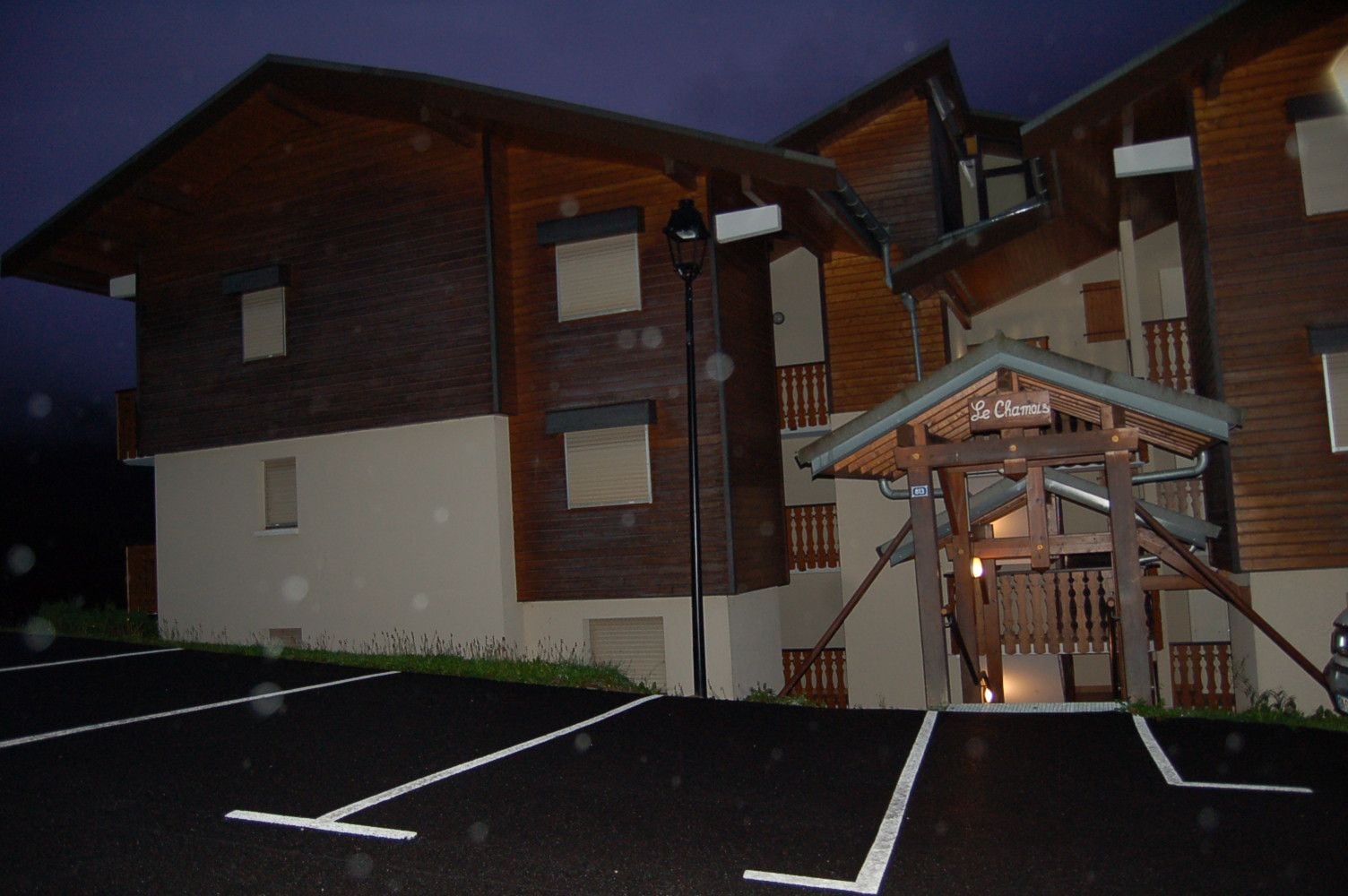 A multi-story building with a wooden facade, a covered entrance, and a parking lot.