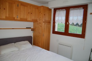 A bedroom with a bed, wooden wardrobe, and a window with a view of a green landscape. - Renovated one-bedroom apartment on the first floor with private parking, 5 minutes from downtown (Châtel)
