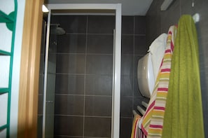A bathroom with a shower, a toilet, and a towel rack with multiple towels. - Renovated one-bedroom apartment on the first floor with private parking, 5 minutes from downtown (Châtel)