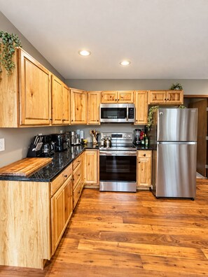 A kitchen with wooden cabinets, stainless steel appliances, and a black countertop. - Chalet Shenanigans • Fireplace • Fire Pit • Game Loft• 4 Bedrooms (Pocono Pines)