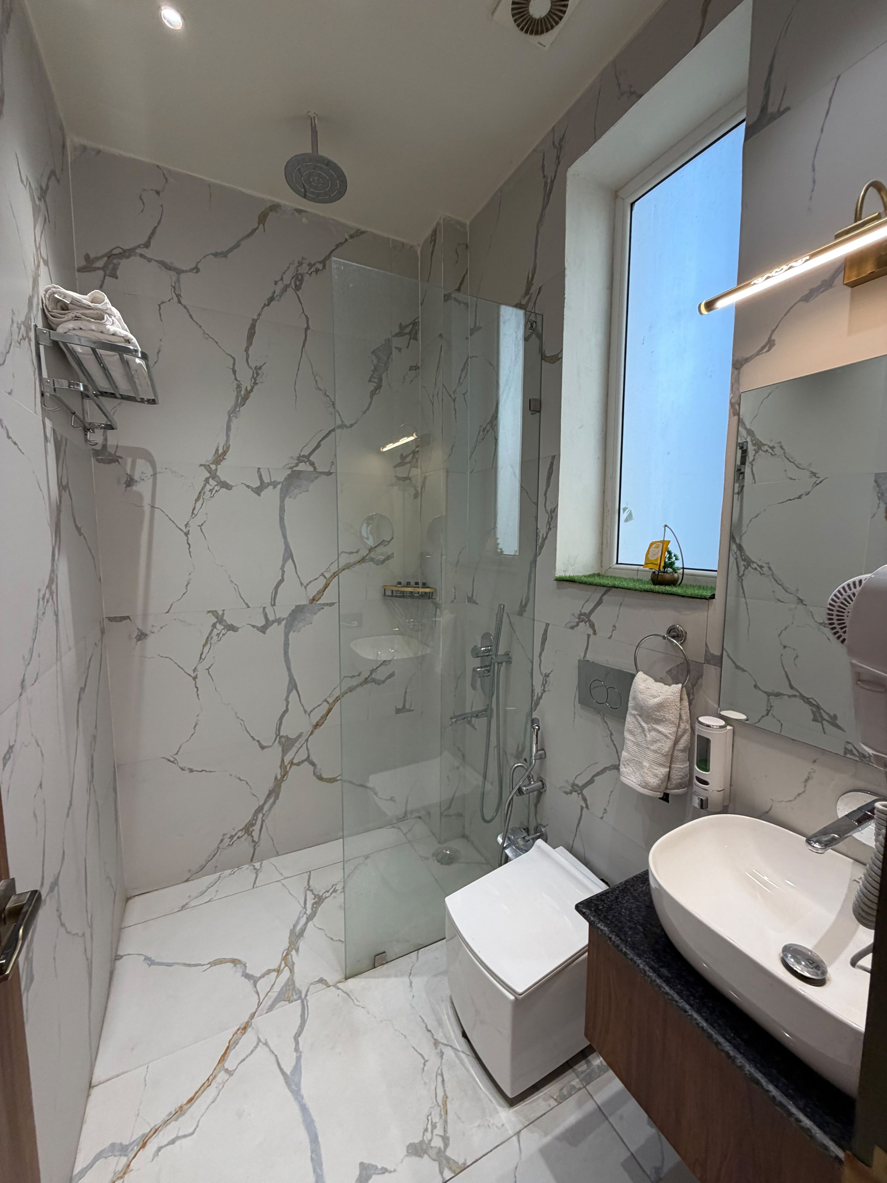 A modern bathroom with a glass-enclosed shower, a white sink, and marble-patterned walls.