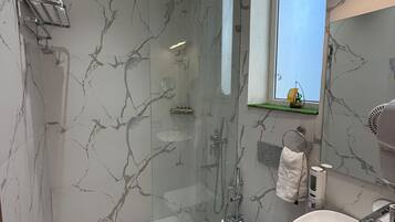 A modern bathroom with a glass-enclosed shower, a white sink, and marble-patterned walls.