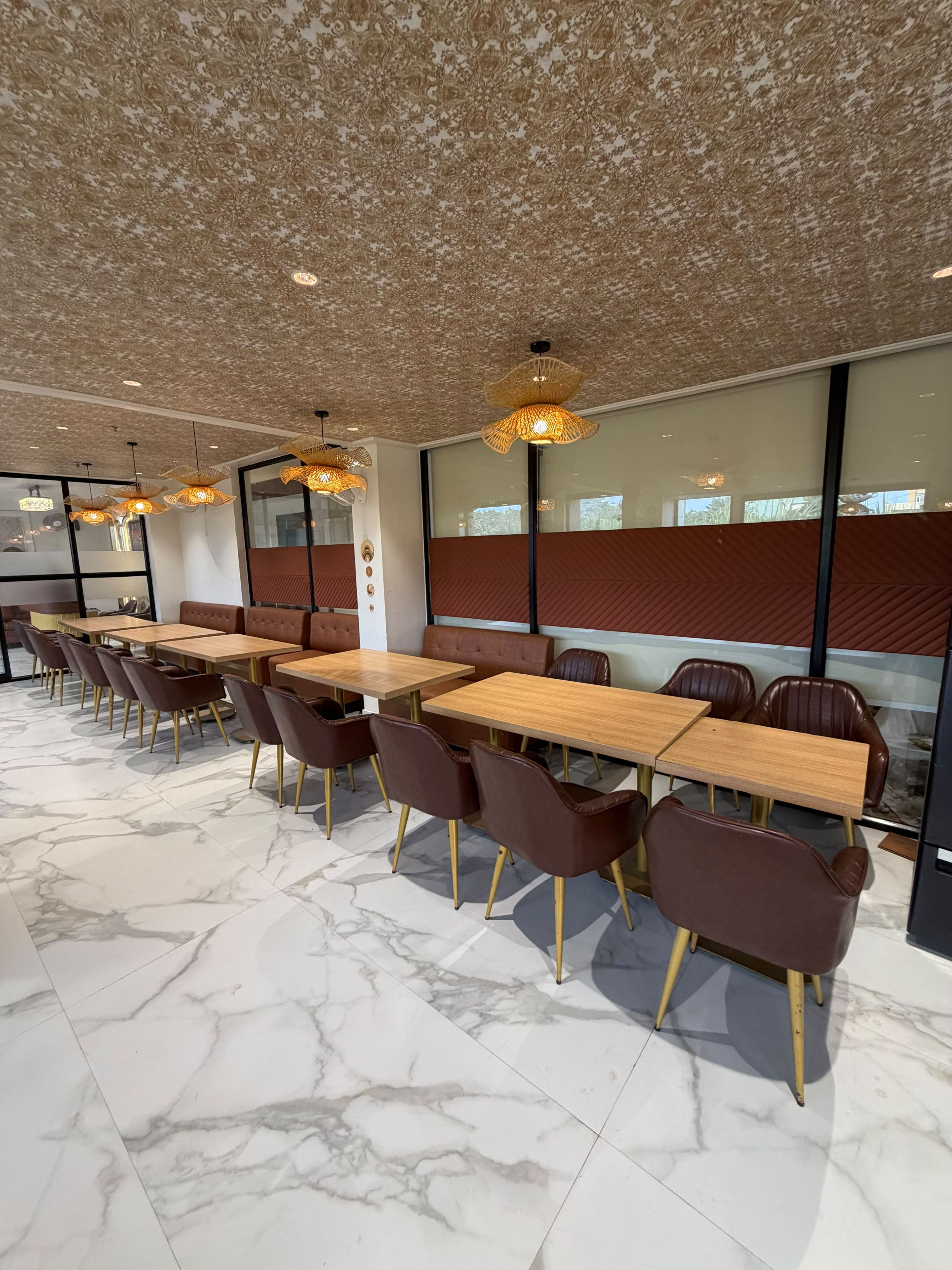 A modern dining area with marble flooring, wooden tables, brown leather chairs, and decorative ceiling lights.
