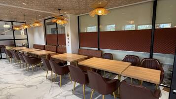 A modern dining area with marble flooring, wooden tables, brown leather chairs, and decorative ceiling lights.