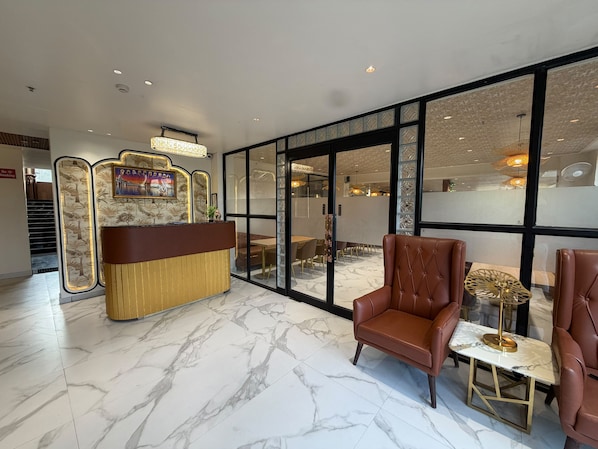 A hotel lobby with a reception desk, seating area, and large windows.