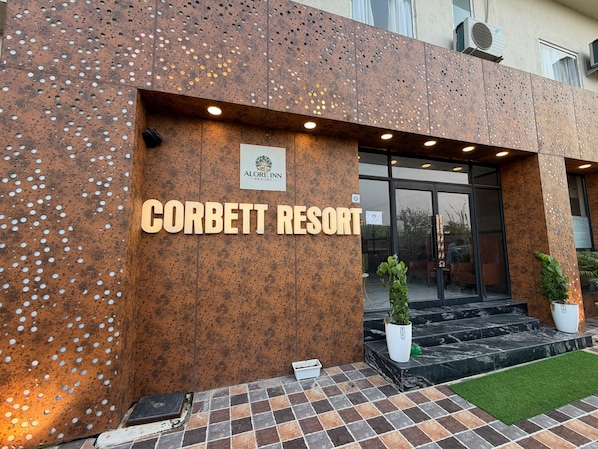 The exterior of Corbett Resort with a signboard, entrance, and potted plants.