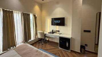 A hotel room with a bed, a desk with a television, a chair, and a small refrigerator.