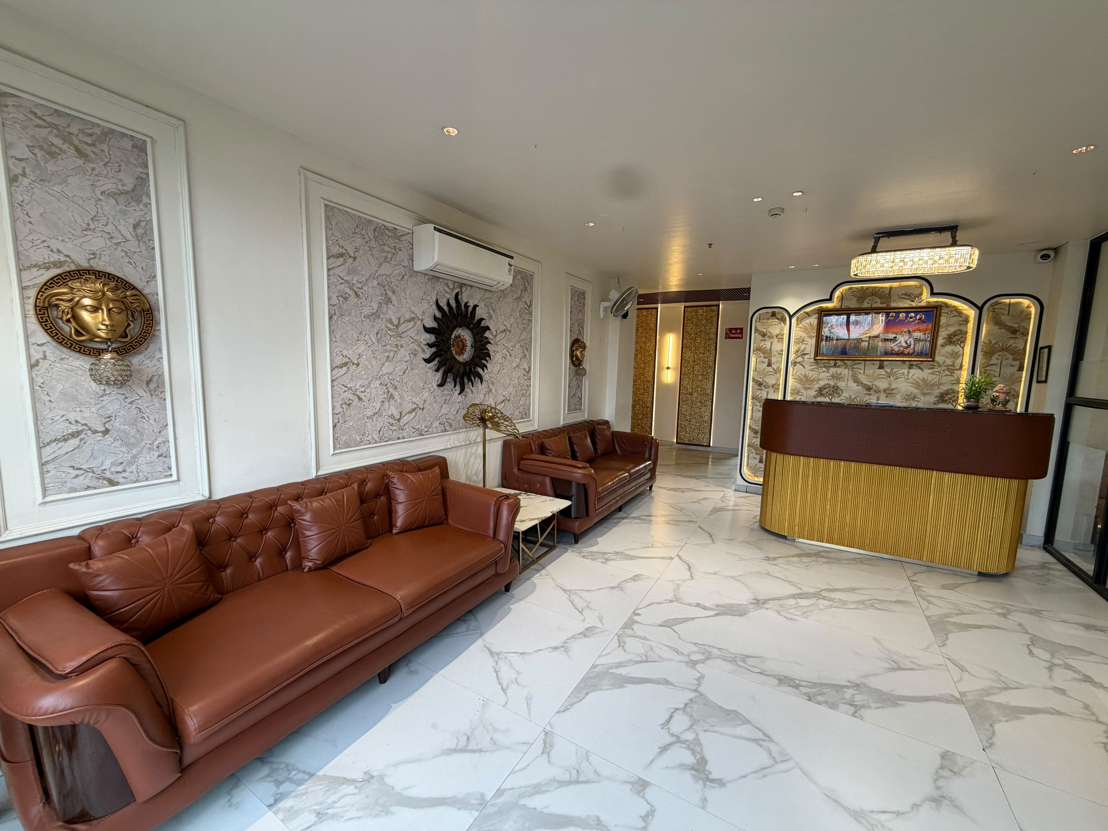A modern lobby with a brown leather sofa, marble flooring, and a reception desk with a decorative backdrop.