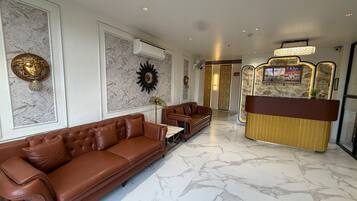 A modern lobby with a brown leather sofa, marble flooring, and a reception desk with a decorative backdrop.