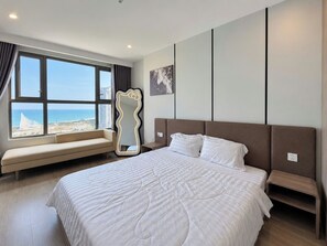 A hotel room with a large bed, a bench by the window, and a view of the sea. - The Song Retreat Apartment-Infinity Pool (Vung Tau)