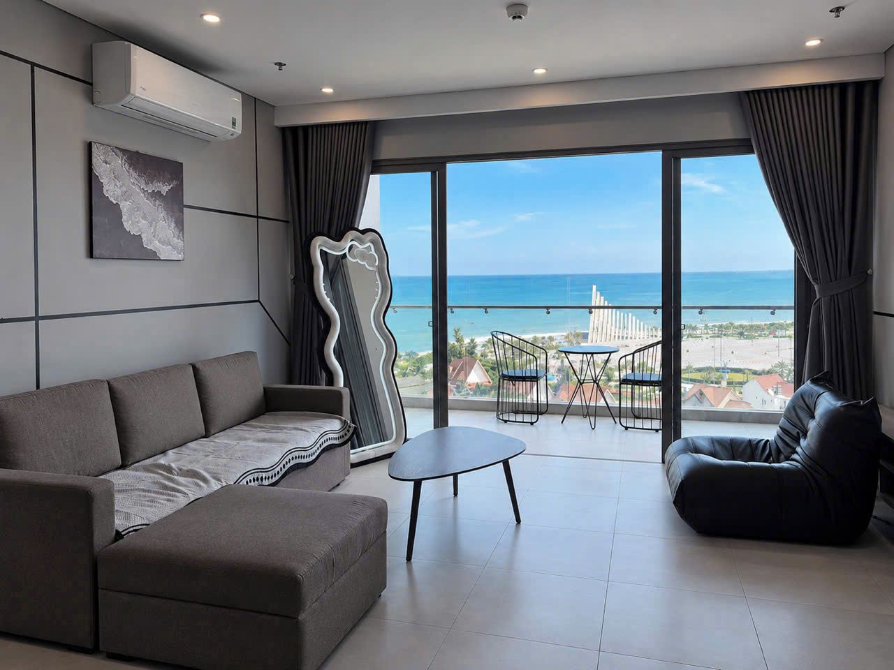 A modern living room with a sofa, a coffee table, and a view of the ocean through large windows.