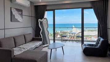 A modern living room with a sofa, a coffee table, and a view of the ocean through large windows.