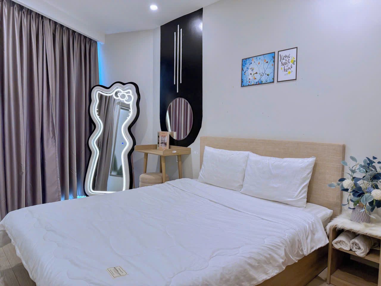 Une chambre d’hôtel avec un grand lit, une table de chevet avec une lampe, un miroir et deux tableaux encadrés au mur.