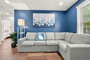 Ein Wohnzimmer mit grauem Ecksofa, einer Stehlampe und einem Wandbild.