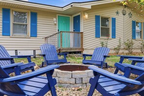 Ein Haus mit Terrasse, nummerierten Türen und blau gestreiften Adirondack-Stühlen, die um eine Steinkaminfeuerstelle angeordnet sind.