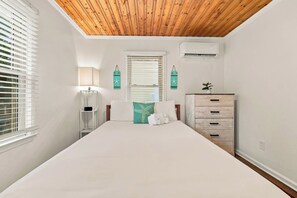 A bedroom with a wooden ceiling, a bed with white bedding, a nightstand, a dresser, and two wall-mounted air conditioning units. - Sea Star One Block to the Beach Top Location (North Myrtle Beach)