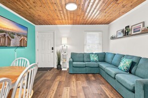 A living room with a wooden ceiling, a teal sofa, a dining table with chairs, and a beach scene painting on the wall. - Sea Star One Block to the Beach Top Location (North Myrtle Beach)
