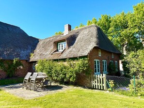 A traditional thatched-roof house with a brick exterior, a small window, and a wooden deck with chairs. - Holiday Home in Oldsum With Swimming Pool (Oldsum)